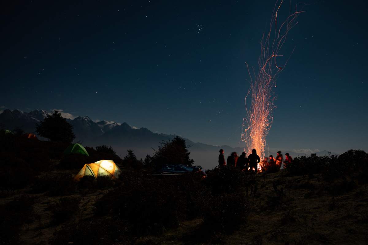 travellers gathered by the campfire on an overnight ridgleline camp in nepal's himalayas
